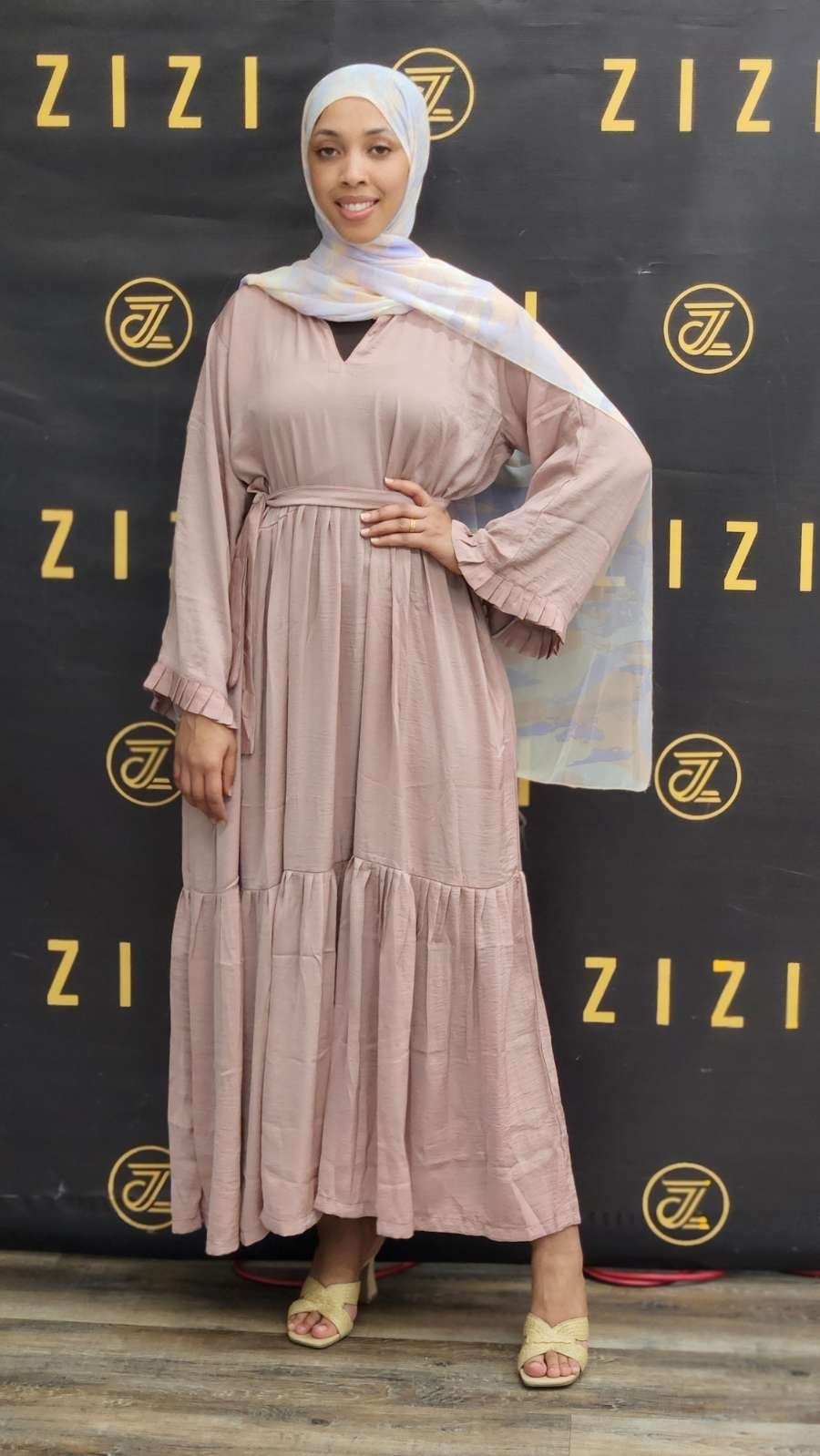 Woman in a long, light-colored dress with a hijab standing in front of a branded backdrop.