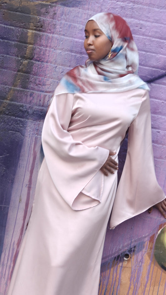 Woman wearing a pale pink Zalina Satin Maxi Dress from ZIZI Boutique with wide bell sleeves and a colorful hijab