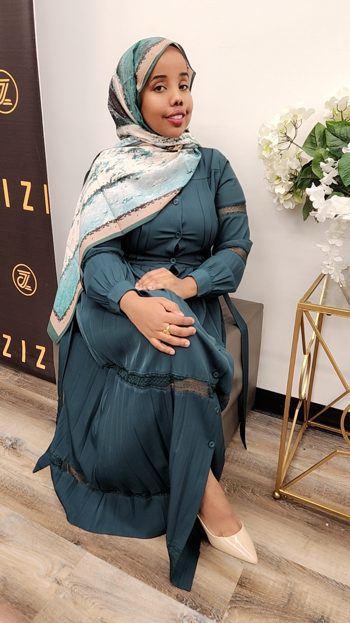 Woman wearing a blue Hodan Lace Maxi Dress from ZIZI Boutique seated indoors with floral decor