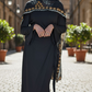 Woman in modest wrap dress wearing a hijab with intricate patterns standing on a street.