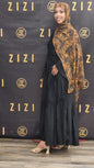 Woman in black dress and patterned hijab standing in front of a ZIZI branded backdrop