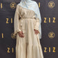 Woman in a beige dress with a light blue hijab standing in front of a branded backdrop.