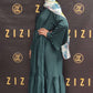 Woman in a green dress and headscarf standing in front of a ZIZI branded backdrop.