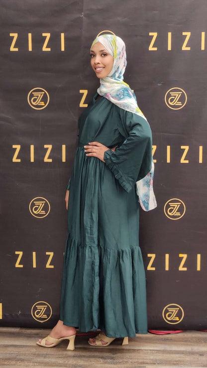 Woman in a green dress and headscarf standing in front of a ZIZI branded backdrop.