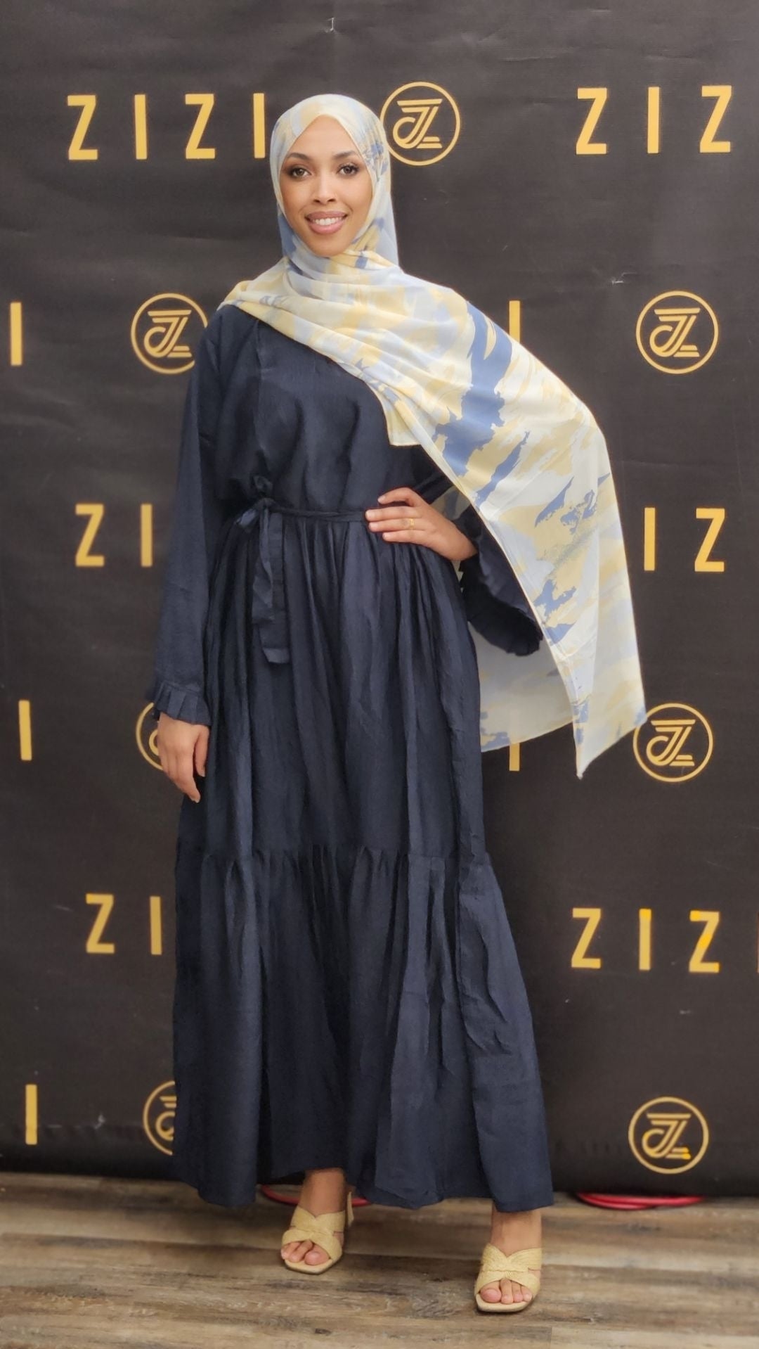 Woman in a navy blue dress with a patterned scarf standing in front of a Zizzi branded backdrop.
