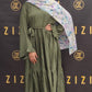Woman wearing a green dress and floral hijab in front of a Zizi branded backdrop