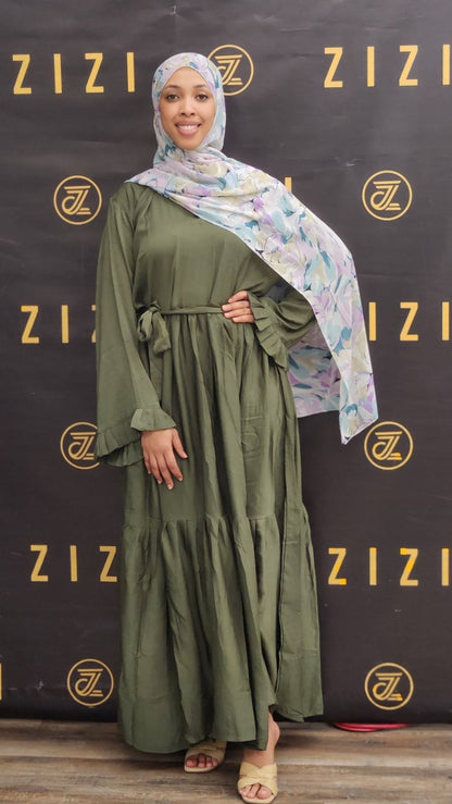 Woman wearing a green dress and floral hijab in front of a Zizi branded backdrop