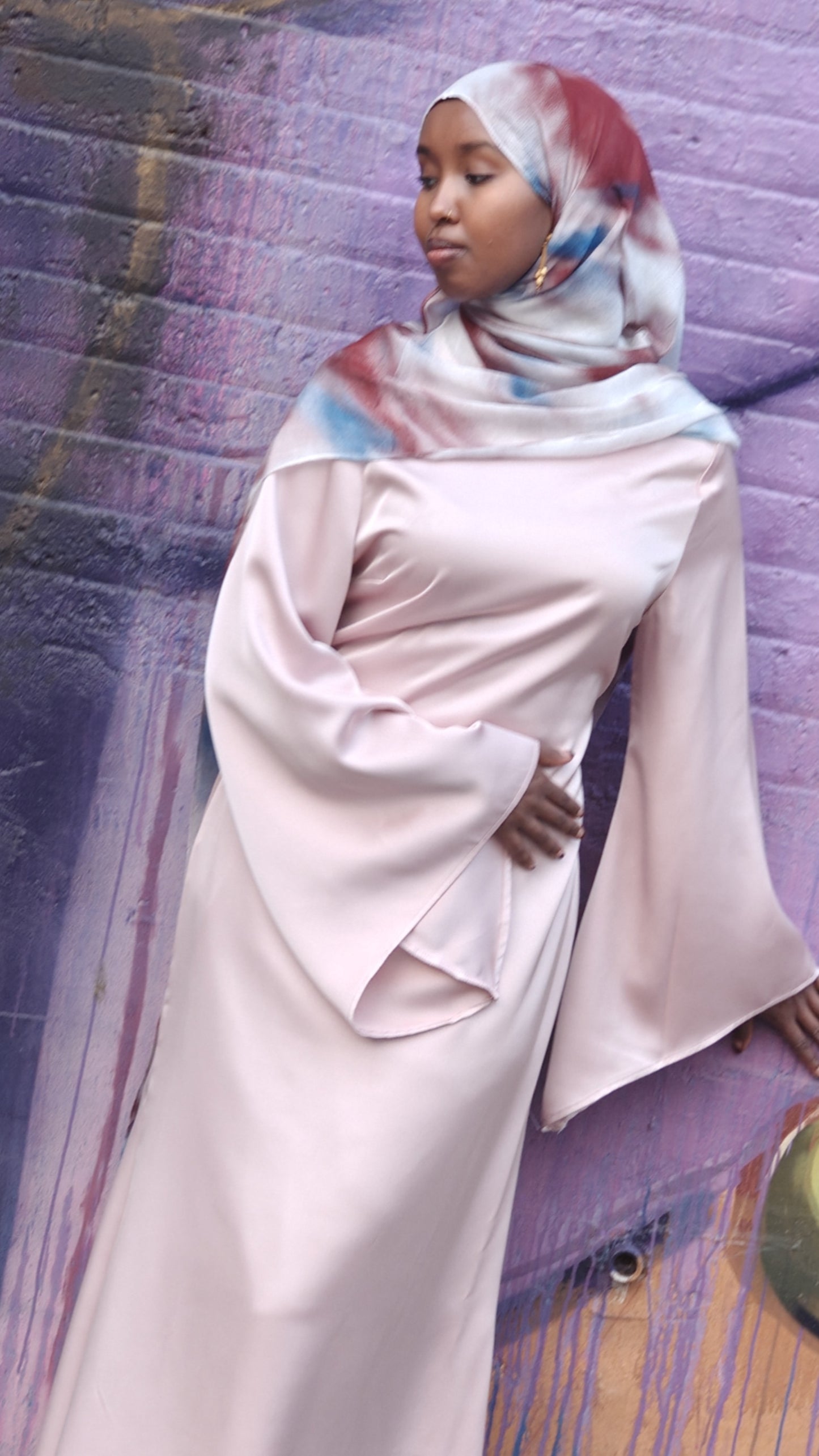 Woman wearing a pale pink Zalina Satin Maxi Dress from ZIZI Boutique with wide bell sleeves and a colorful hijab