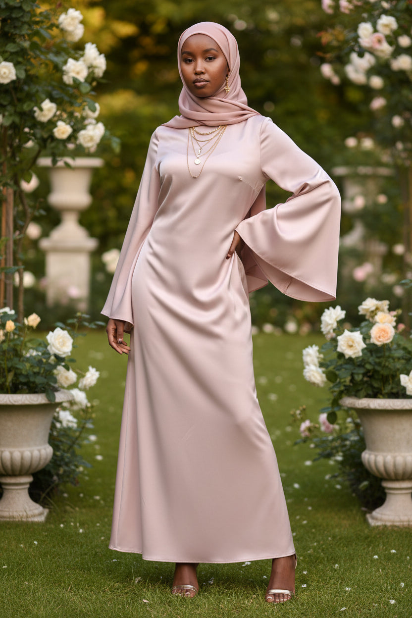 Woman wearing a pale pink Zalina Satin Maxi Dress from ZIZI Boutique with wide bell sleeves and a colorful hijab