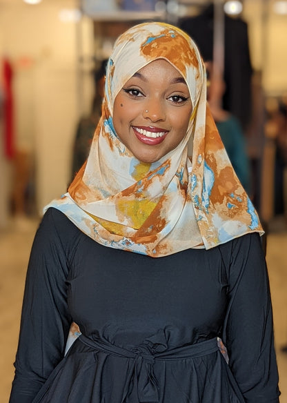 Smiling woman wearing ZIZI Boutique chiffon print hijab Carmel Yellow Light Blue Ink Blots with a stylish dark outfit