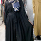 Woman wearing black pleated button down dress with a belt, styled with patterned headscarf in boutique
