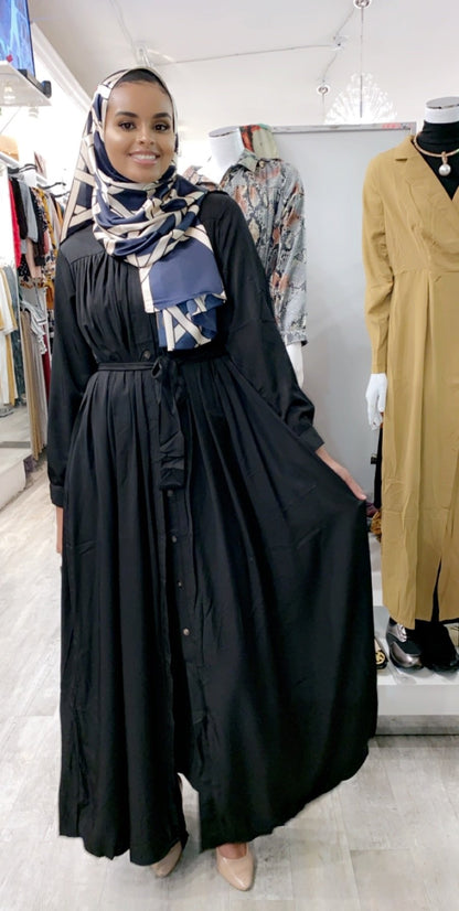 Woman wearing black pleated button down dress with a belt, styled with patterned headscarf in boutique